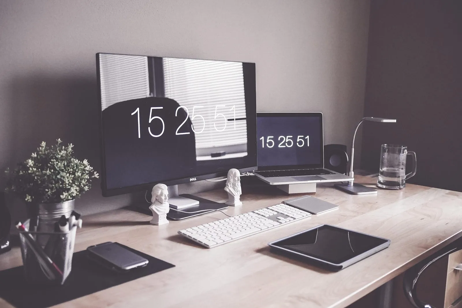 Meja kerja kayu dengan tablet, keyboard putih, monitor, laptop, dan ponsel
