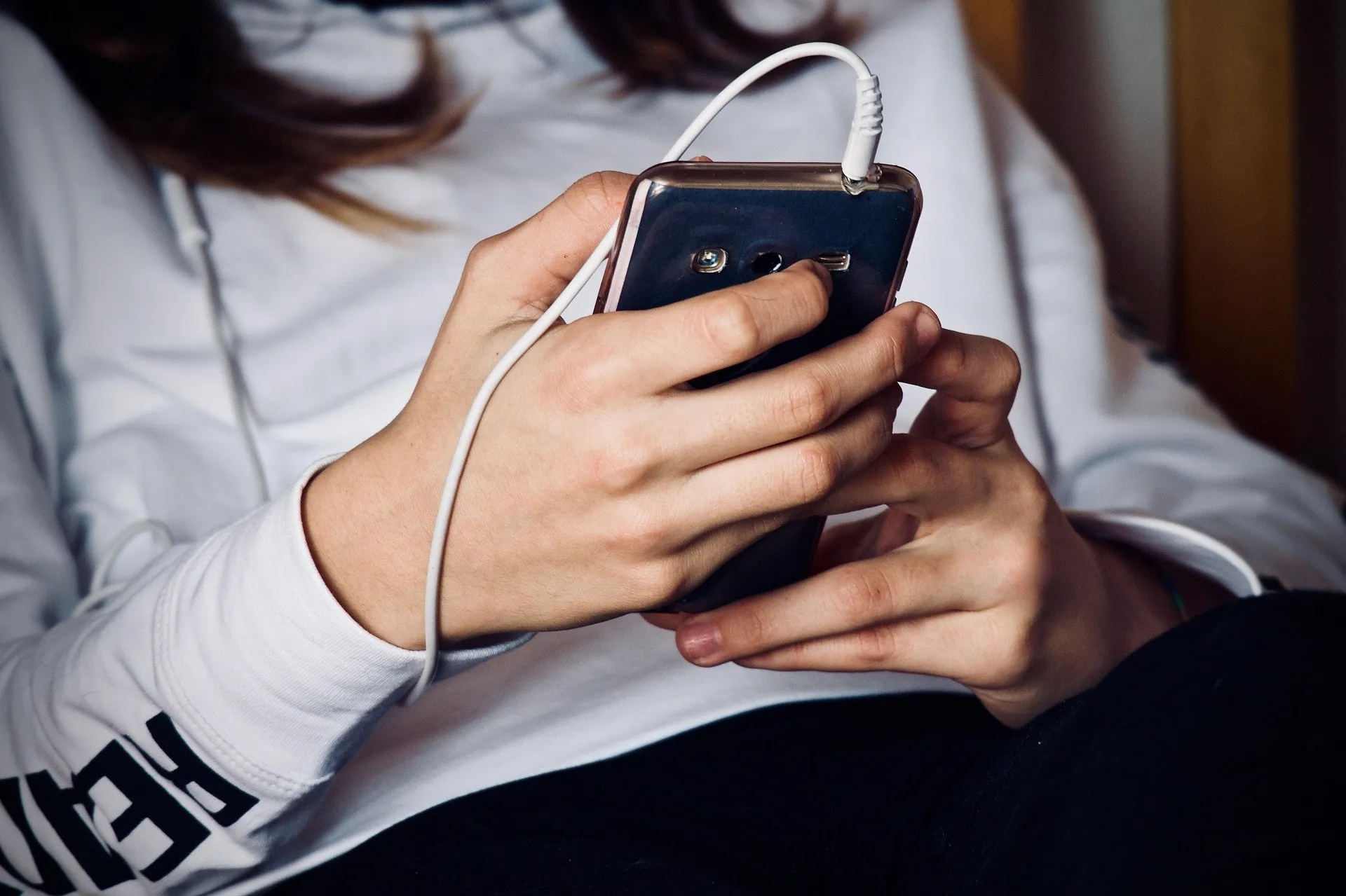 Seseorang memegang ponsel dengan kabel earphone terpasang